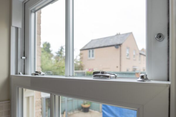 A white uPVC sash window installed in a home, viewed from inside with the catch and lock visible and houses outside