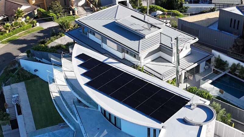 Aerial view of a large modern curved-roof home with black solar panels installed on the roof