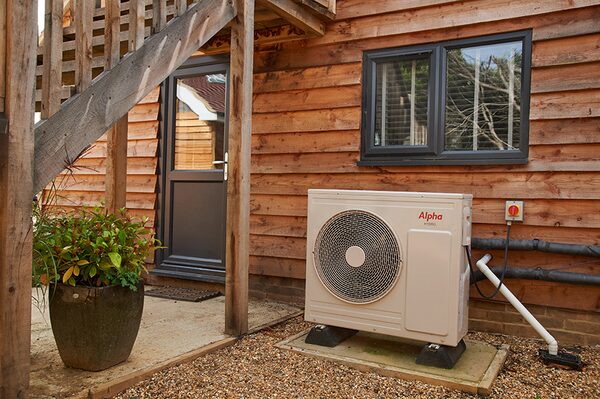 An Alpha heat pump installed outside a wooden-clad house next to a door and window