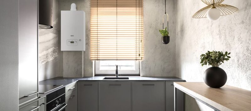 A white Baxi wall-mounted combi boiler installed in a modern grey kitchen beside a window with wooden blinds
