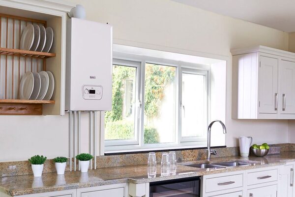 A white Baxi wall-mounted system boiler installed in a bright cream kitchen above a granite worktop next to a window