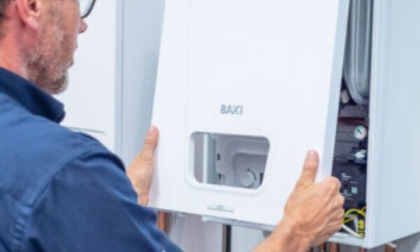 An engineer refitting the white front casing of a Baxi wall-mounted gas boiler during a service