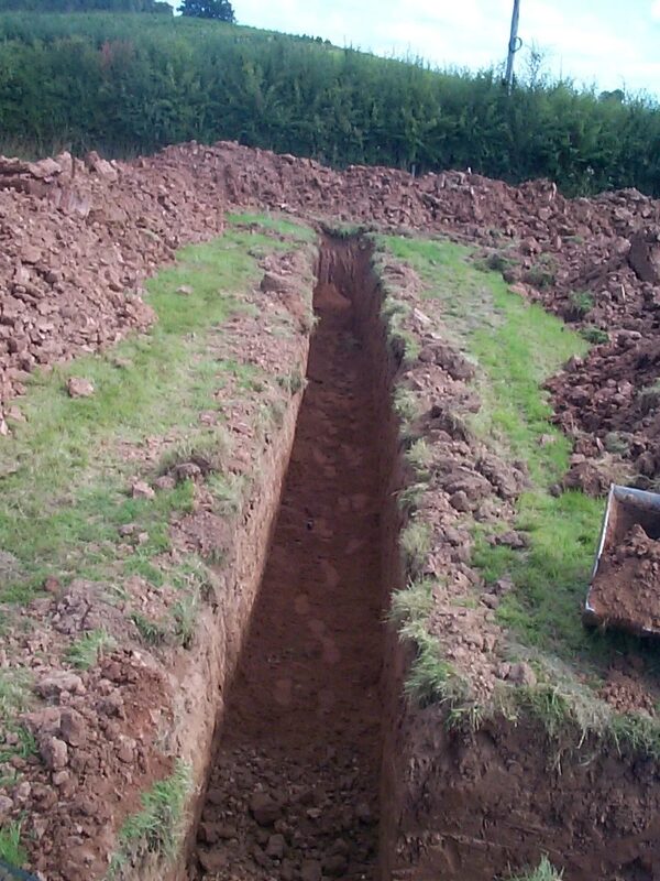A long excavated trench dug in a grassy field for a ground source heat pump ground loop installation