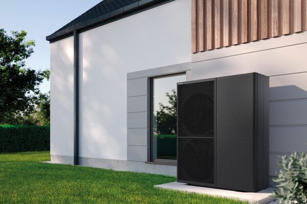 A dark grey Panasonic air source heat pump unit installed on the exterior wall of a modern house beside a window and lawn.