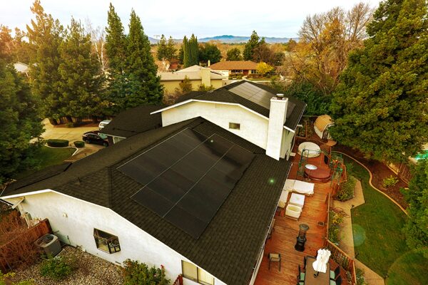 Aerial view of a suburban house with all-black solar panels installed on its shingled roof