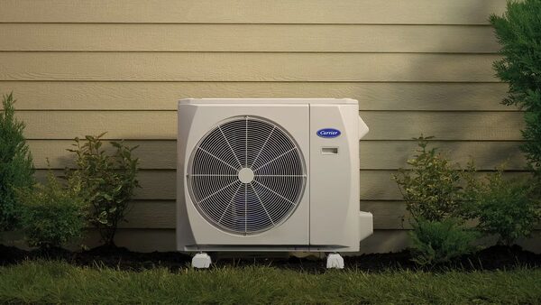 A Carrier outdoor heat pump unit installed on grass against the tan siding of a house