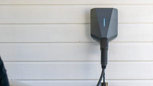 A dark grey Easee One wall-mounted EV charger with a blue indicator light and tethered cable on a white timber-clad wall