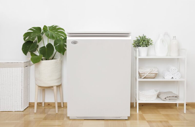 A white Grant Vortex oil boiler standing in a bright utility room beside a plant and shelving with towels and bottles