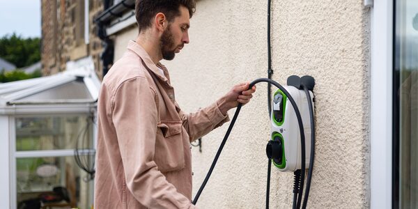 A man plugging the cable into a wall-mounted green and white EV chargepoint outside a house