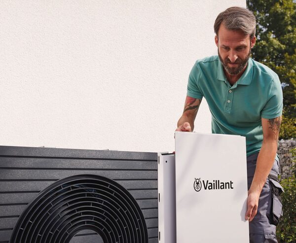 An installer fitting the front panel onto a Vaillant aroTHERM split air source heat pump outside a house