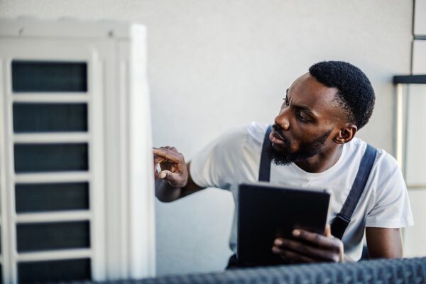 A technician holding a tablet inspects an outdoor air source heat pump unit