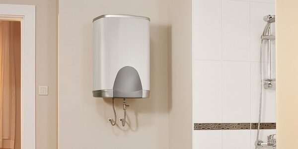 A white wall-mounted electric water heater/boiler unit installed in a bathroom next to a tiled shower wall