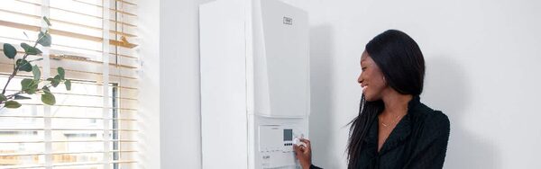 A woman adjusting the controls of a white wall-mounted Ideal combi boiler next to a window with blinds