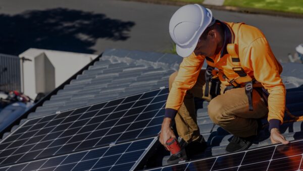 A worker in an orange hi-vis jacket and white hard hat installing solar panels on a tiled roof