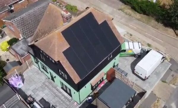 Aerial view of a UK house with black solar panels installed on its roof and vans parked in the driveway