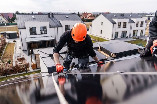 A worker in an orange hard hat and safety harness installing solar panels on a residential roof