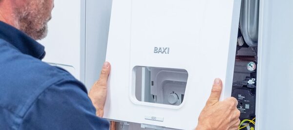 A technician fitting the white front casing onto a Baxi wall-mounted gas boiler