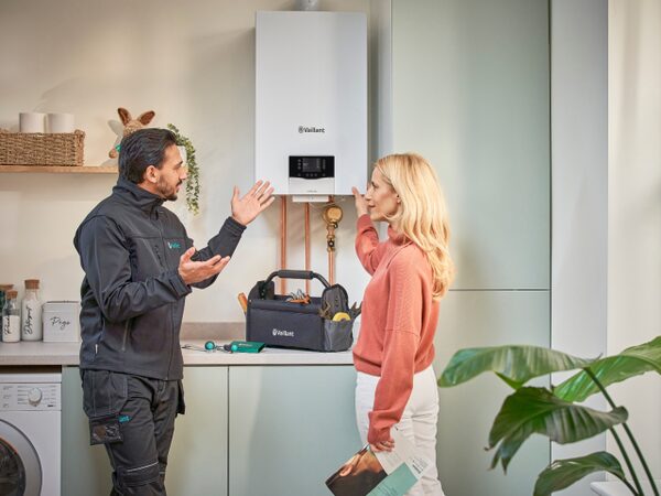 A Vaillant engineer talking to a woman beside a wall-mounted Vaillant boiler in a kitchen