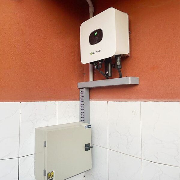 A white Growatt solar inverter mounted on an orange wall above a grey electrical distribution box