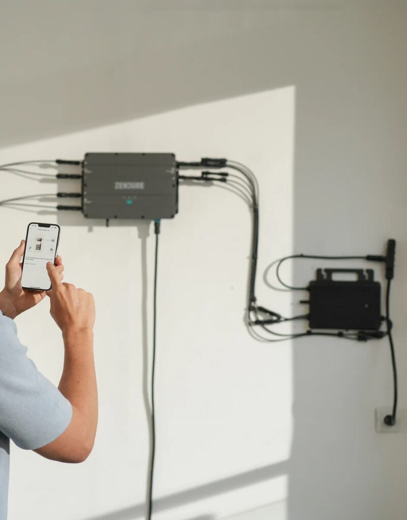 A person using a smartphone app to control a Zendure wall-mounted solar microinverter and battery unit installed on a white wall