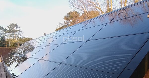A large in-roof solar panel array installed on a sloping roof, with trees reflected in the glossy panels