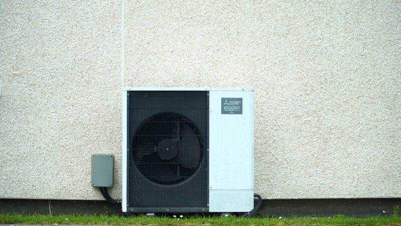 A Mitsubishi Ecodan air source heat pump unit installed against the exterior wall of a house