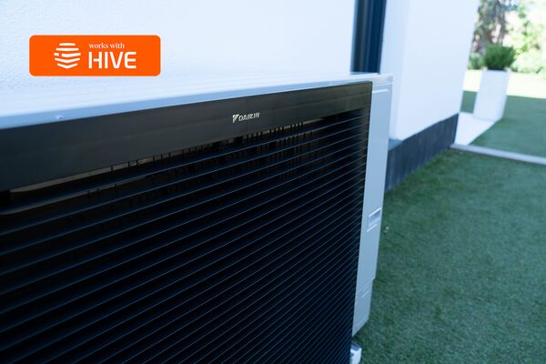 A Daikin air source heat pump outdoor unit installed outside a house, with a 'works with Hive' badge overlaid