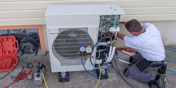 A technician installing an air source heat pump unit outside a house, with tools and pressure gauges around it
