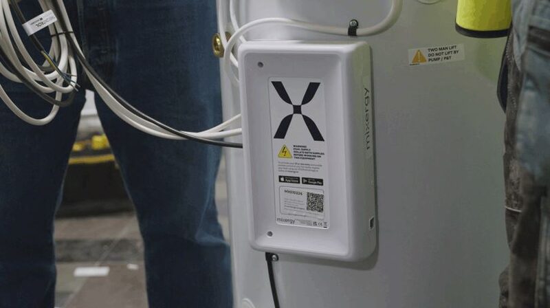 A Mixergy hot water cylinder with its white controller unit mounted on the tank during installation