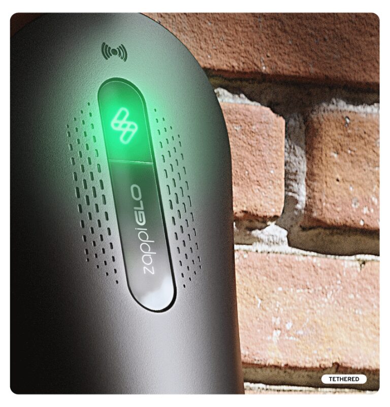 Close-up of a myenergi zappi GLO EV charger mounted on a brick wall with a green glowing status light