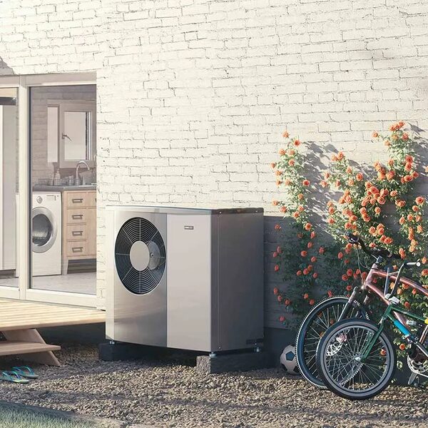 A NIBE air source heat pump installed outside a house wall beside bicycles and climbing roses