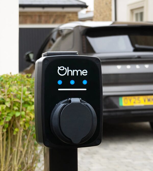 An Ohme wall-mounted EV charge point installed on a driveway with a dark Volvo car parked behind it