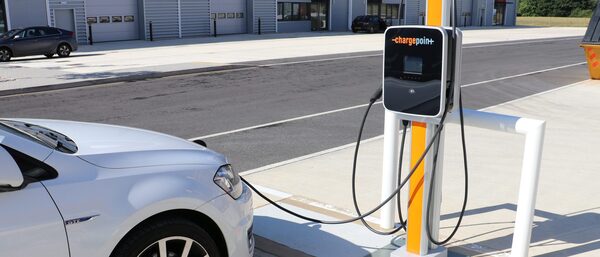 A white car plugged into a ChargePoint public EV charge point in a car park