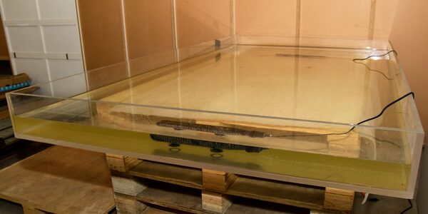 A solar panel submerged in a large water-filled acrylic tank in a laboratory, used for testing