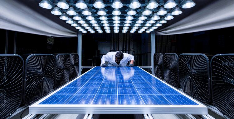 A technician inspecting a solar panel under a bank of test lamps in a laboratory testing rig