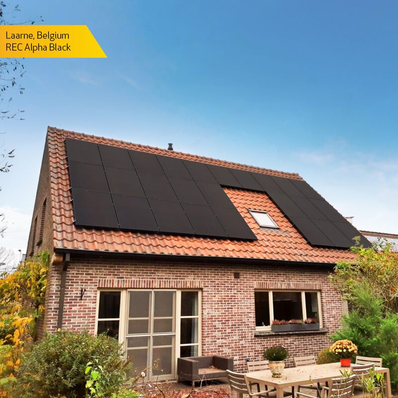A brick house with black REC Alpha Black solar panels on its tiled roof, with a yellow label reading 'Laarne, Belgium REC Alpha Black'