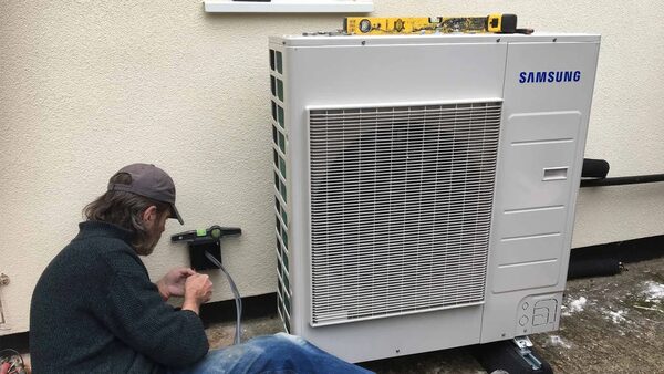 An engineer working beside a Samsung air source heat pump installed outside a house wall