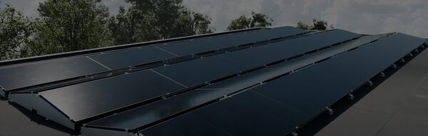 Rows of dark solar panels mounted on a flat roof with a mounting system, against a cloudy sky