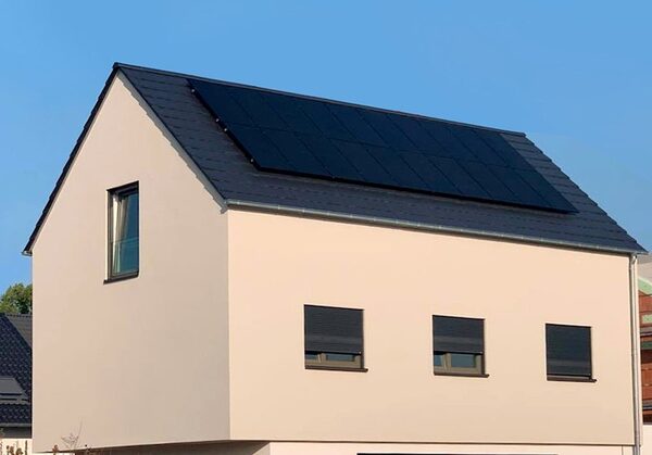 A cream-coloured house with black monocrystalline solar panels installed on its dark tiled roof
