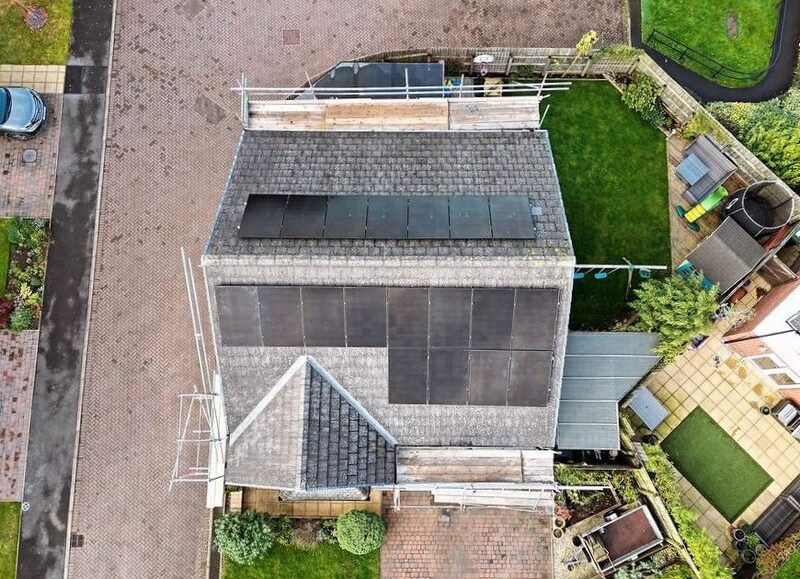 Aerial view of a UK house roof with two arrays of black solar panels installed, surrounded by scaffolding