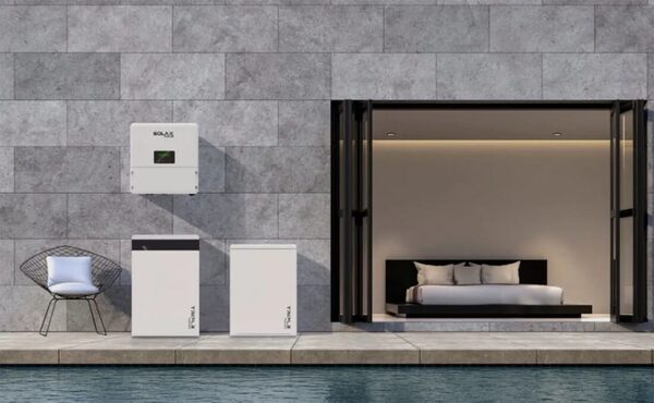 SolaX wall-mounted inverter and two floor-standing battery units installed on a grey tiled wall beside a modern bedroom