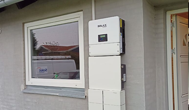 A SolaX battery inverter and battery storage units mounted on the exterior wall of a house next to a window