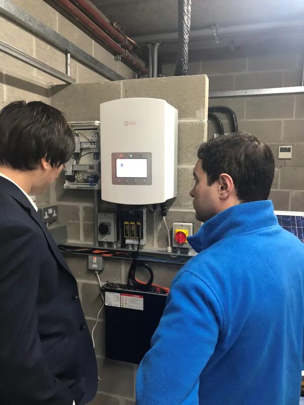 Two men inspecting a wall-mounted Solis hybrid inverter and battery installation in a plant room