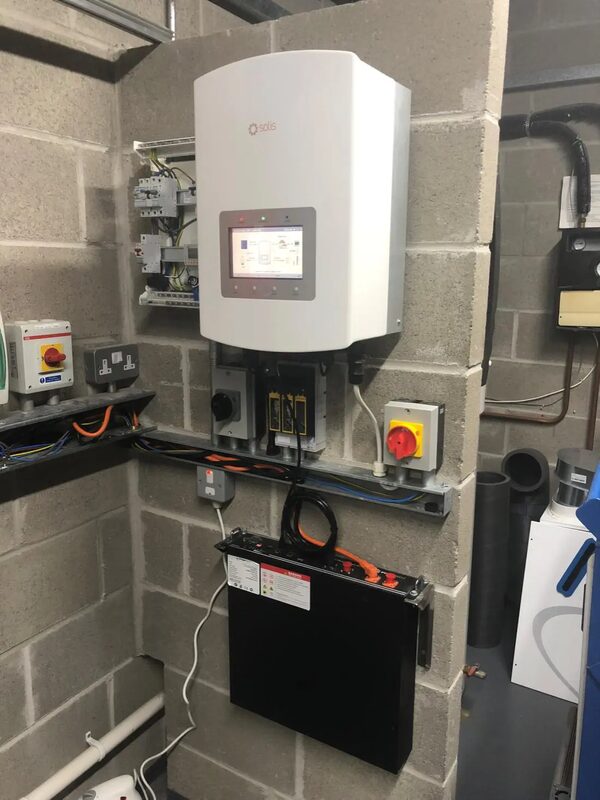 A Solis hybrid inverter and wall-mounted battery installed on a concrete block wall in a plant room