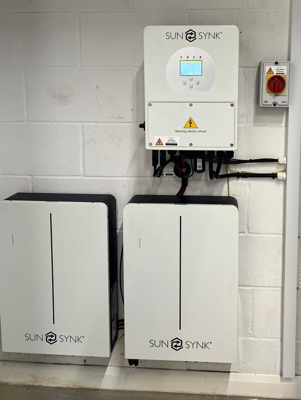 A Sunsynk hybrid inverter and two Sunsynk battery units wall-mounted on a white brick wall