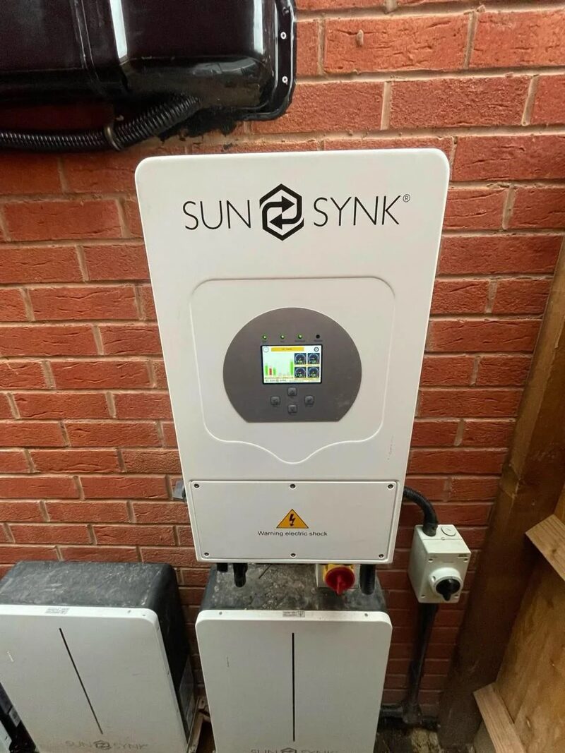 A Sunsynk hybrid inverter and battery storage units installed on a brick wall outside a house