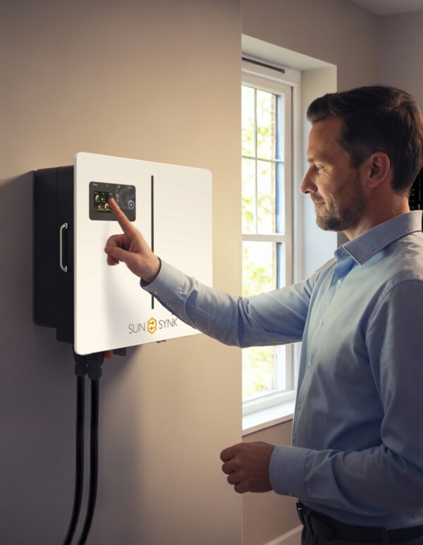 A man touching the display of a white Sunsynk wall-mounted home battery inverter installed indoors next to a window