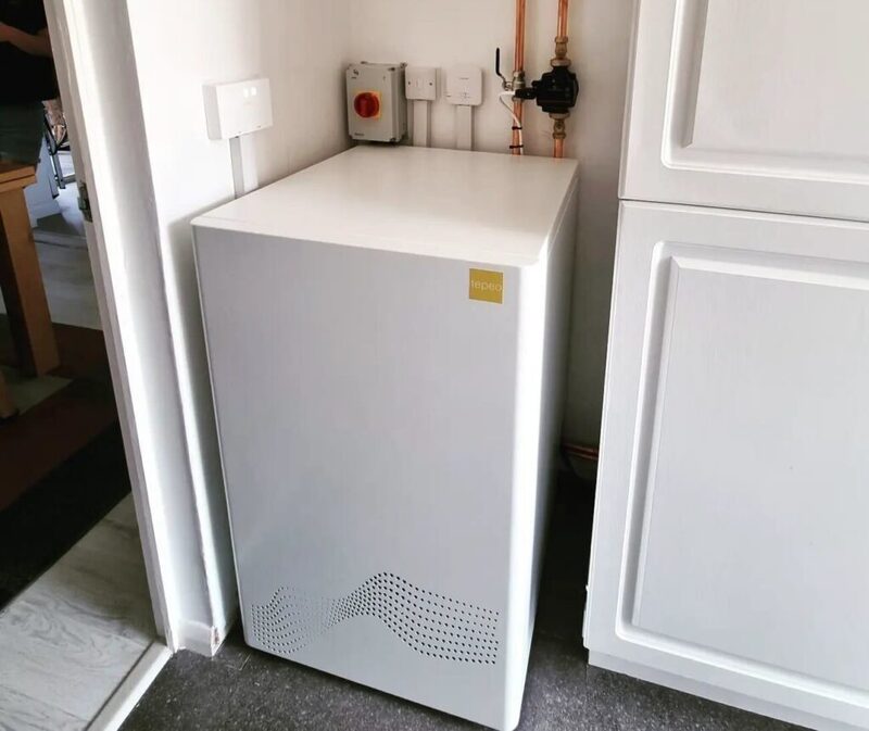 A white Tepeo heat battery boiler installed in a corner of a home next to copper pipework and electrical controls