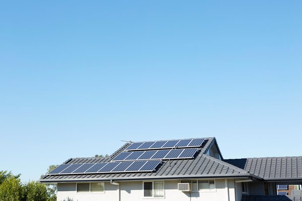 Solar panels installed on the tiled roof of a suburban house under a clear blue sky