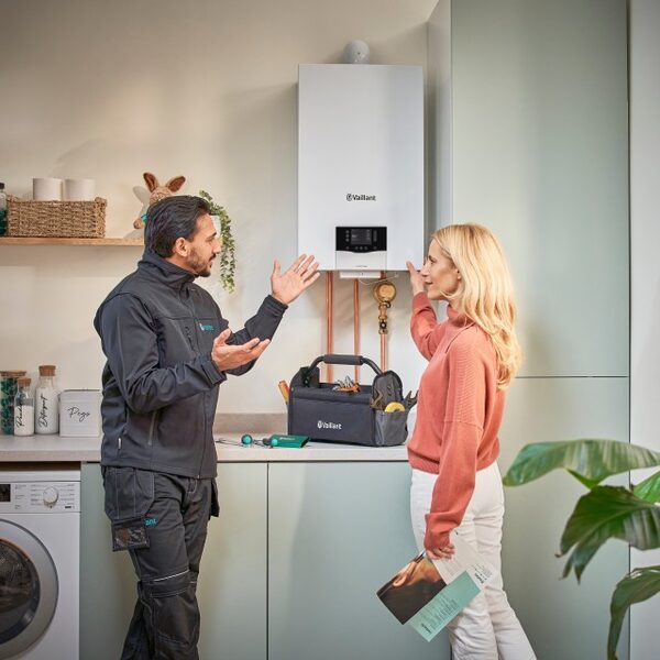 A Vaillant engineer explaining a wall-mounted Vaillant boiler to a woman in a kitchen